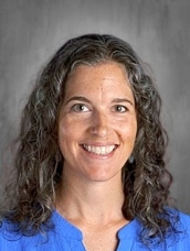 Smiling woman with long, curly hair wearing a blue shirt, set against a neutral background.