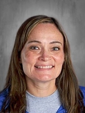 Smiling woman with long brown hair, wearing a blue shirt, against a gray background.