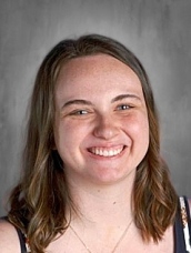 Smiling young woman with shoulder-length brown hair, wearing a floral top, against a gray background.