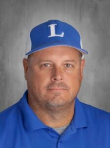 A man with a short beard wearing a blue polo shirt and blue cap, featuring the letter "L," poses for a portrait.