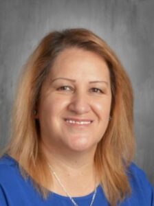 Portrait of a woman with light brown hair, smiling, wearing a blue shirt against a gray background.