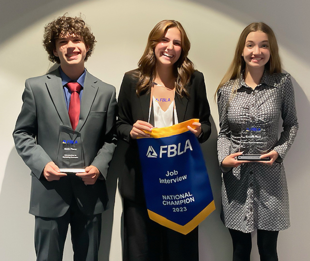 Monty Puttroff, Malia Hendricks, and Ella McGregor dressed in suits and a dress, standing in a row, and holding the awards they won at FBLA. Smiling at the camera. 