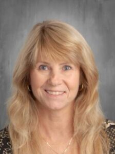 A smiling woman with long, blonde hair and a patterned top poses for a headshot against a gray background.